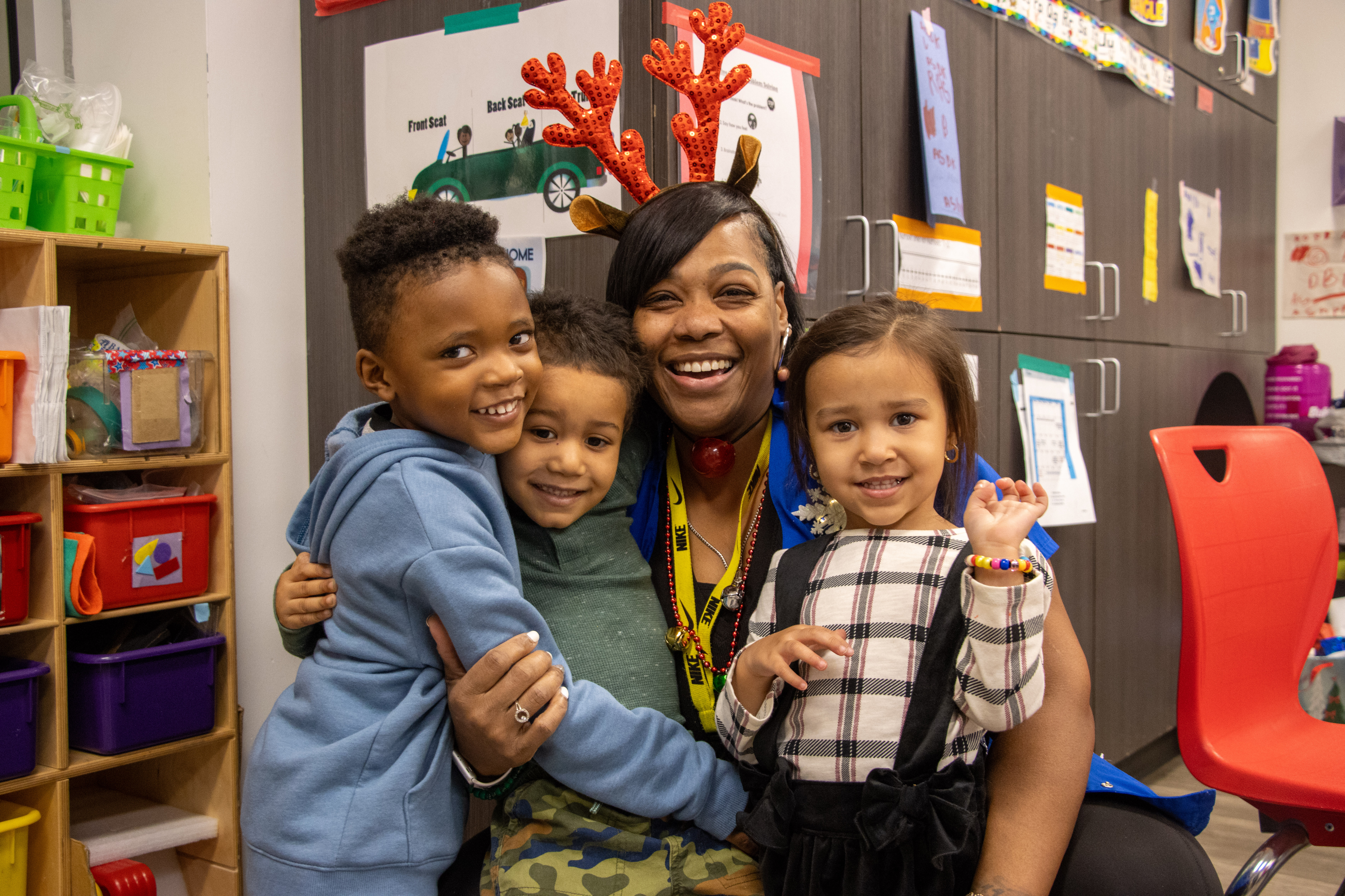 A teacher and her three young students hugging and dressed up for the holidays