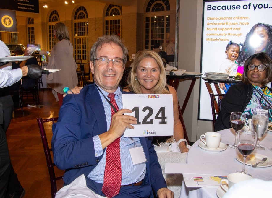 A man and a woman sit together holding up a paddle they raised in an auction