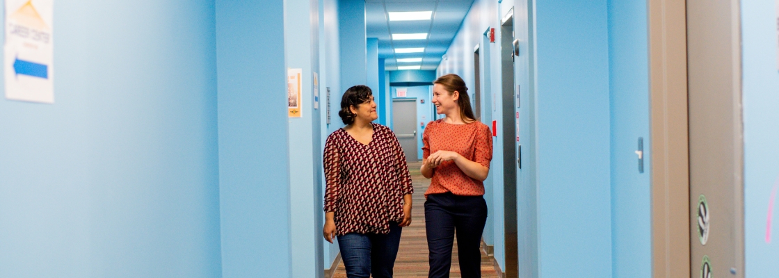 two smiling people walking down a blue hallway while talking
