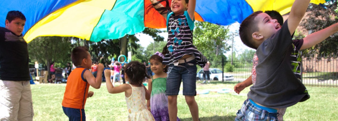kids playing outdoors with a multicolored parachute 