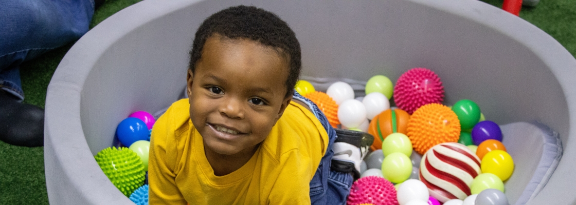 young boy playing in an oversized bowl full of colorful balls