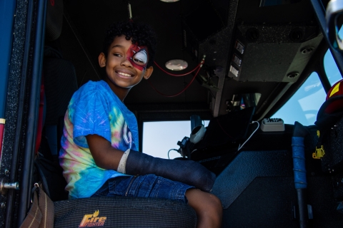  A boy with spider man face painting sitting on a firefighter truck