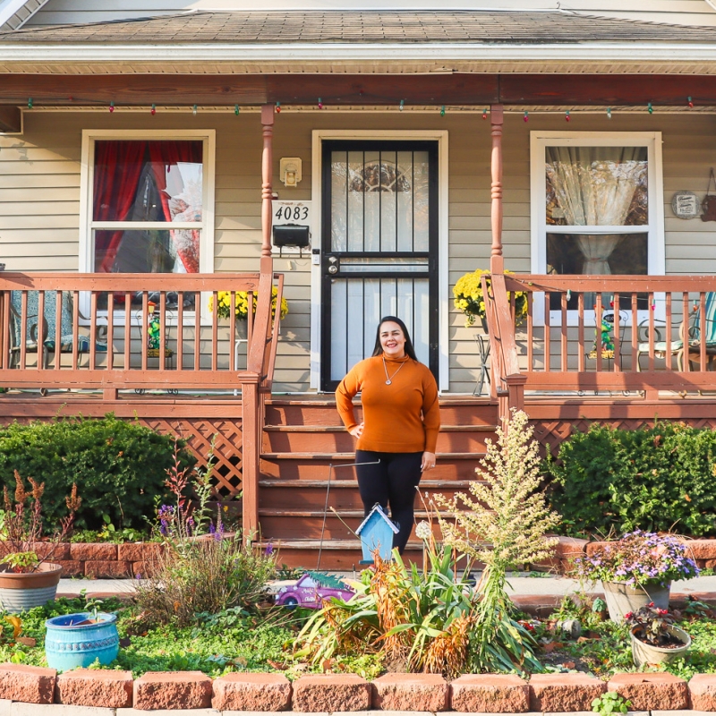 a woman stands outside her home surrounded by her garden