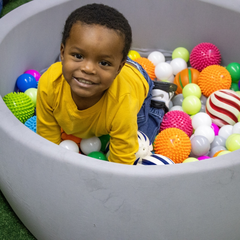 young boy playing in an oversized bowl full of colorful balls