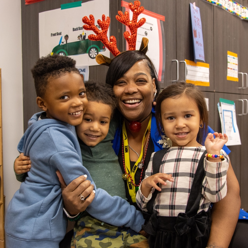 A teacher and her three young students hugging and dressed up for the holidays