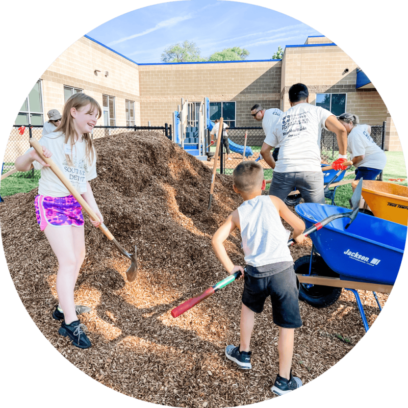 A group including kids working on moving mulch to cover playground floor