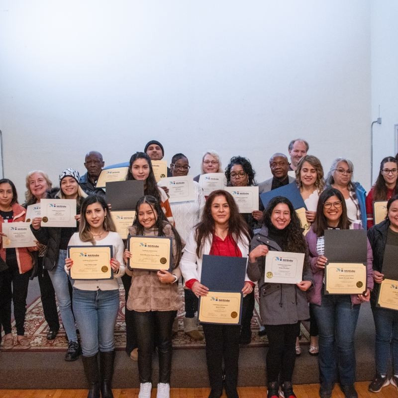 Adult students standing together with certificates of completion or achievement in their GED and ESL programs