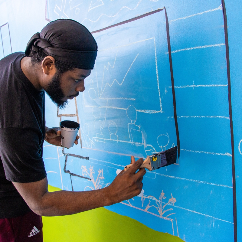 Man paints a mural on a blue wall