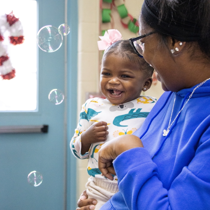 Young child being held by adult looking at bubbles. 