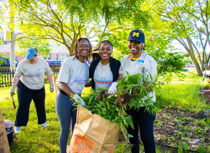 three women smiling and loading branches into a yard bag at Neighborhood Beautification Day 2024
